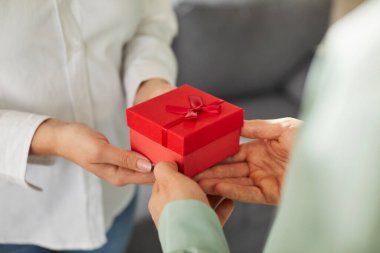 İki kişi, erkek ve kadın eli kırmızı kurdeleli hediye kutusunu tutuyor. Aşk atmosferi, karşılıklı anlayış, uyum, aile ilişkileri. Doğum günü hediyesi, Sevgililer Günü, Noel, Yeni Yıl.