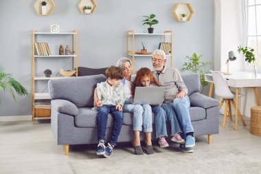 Torunları olan büyük anne ve babaları kanepede yan yana oturmuşlar. Bilgisayarla video görüşmesi yapıyorlar ya da film izliyorlar. Gülümseyen yaşlılar, çocuklar hafta sonunun keyfini çıkarırken evdeki kanepede dinleniyorlar..