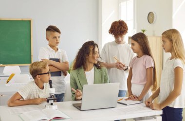 Öğretmen bilgisayarı kullanıyor, modern teknolojiyi okulda öğreniyor. Pozitif ve ilgili öğrencilerle çevrili bu grup, okul ortamındaki eğitime odaklandı..