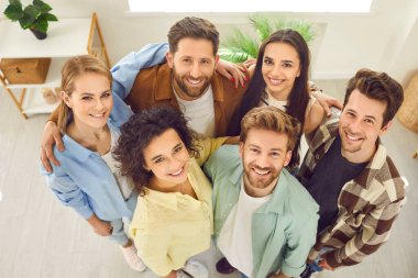 Bir grup mutlu, gülümseyen genç arkadaşın resmi. Günlük giysiler içindeki öğrenciler ya da meslektaşlar. Evde bir arada duruyorlar ve kameraya güvenle ve olumlu bir şekilde bakıyorlar..