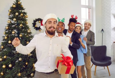 Ev partisinde Noel ağacında dans eden mutlu arkadaşlar. Noel Baba şapkası ve saç bandı takmış neşeli insanlar birbirlerinin arkasındayken eğleniyorlar. Noel ve Yeni Yıl Kutlaması