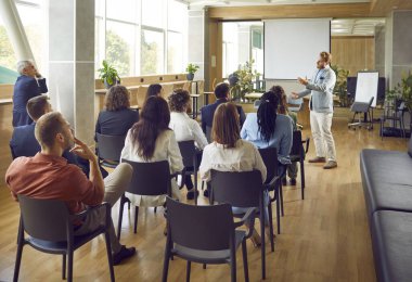 Ofiste, çok ırklı şirket çalışanlarının ya da bir grup personelin önünde oturup liderlerini dinleyen kendine güvenen bir iş adamı..