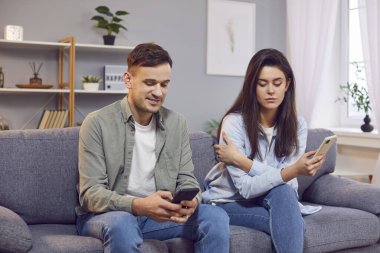 Kadın, adamın akıllı telefonuna gizlice bakıp mesajlarını dinliyormuş. Çift koltukta ellerinde akıllı telefonlarla oturuyor. Dijital çağda gizlilik ve ilişki dinamiği kavramı