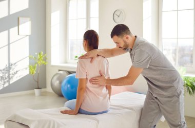 Erkek osteopat modern ofiste genç bir kadını muayene ediyor. Genç fizyoterapist rehabilitasyon kliniğinde bir kadını iyileştiriyor. Kayropraktik uzmanı omurga eğriliği ve sırt ağrısı olan hastaya yardım ediyor..