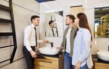 Mutlu çift banyo mobilyaları ve tesisat malzemeleri alıyor ve birlikte yeni bir leğen seçiyorlar. Hijyenik eşya dükkanındaki gülümseyen tezgahtar çeşitli modern beyaz lüks lavaboları gösteriyor.
