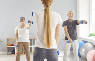 Yaşlı yetişkin insanlar spor salonunda halterlerle spor yapıyor. Spor salonunda spor yapıyor. Rehabilitasyon dersinde spor yapan son sınıf öğrencileri. Sağlıklı yaşam tarzı ve emeklilik kavramı.