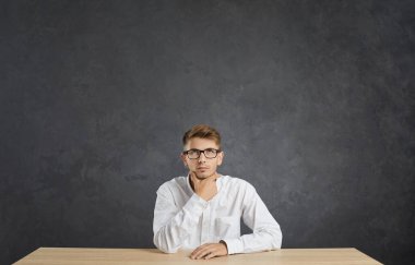 Yansımalar. Ciddi bir beyaz adamın portresi. Gri arka planda dalgın bir ifade var. Tişörtlü ve gözlüklü bir adam masaya oturmuş önemli şeyler düşünüyor ya da karar veriyor..