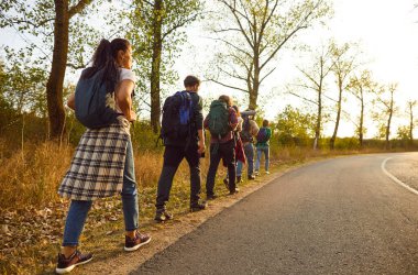 Bir grup turist sıcak bir eylül gününde yürüyüşe ya da yürüyüşe çıkıyorlar. Sırt çantalı gençlerden oluşan bir ekibin yol kenarında yeşil ağaçlarla kaplı bir yolda birlikte yürümesini izleyin.
