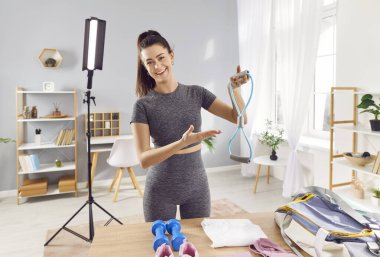 Mutlu bir kadının portresi, bir fitness koçu ve blog yazarı, evde spor malzemelerini kullanarak online eğitim oturumları düzenleyen veya video blogları kaydeden. Spora ve forma odaklanıyor..
