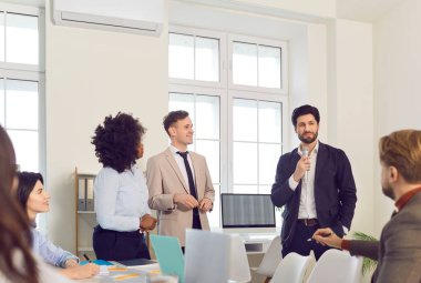 İş koçu, modern ofis ortamında antrenman sırasında katılımcılarla meşgul oluyor. Çok ırklı insanlar mikrofon tutan adamı dinler ve profesyonel gelişim hakkında emin bir şekilde konuşurlar..