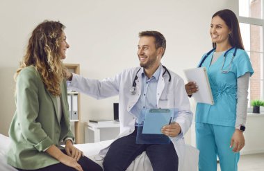 Gülümseyen dost canlısı hemşire ve erkek doktor, kendisini destekleyen ve tedavisini klinikte tartışan hasta kadınla konuşuyor. Tıbbi muayene ve sağlık konsepti.