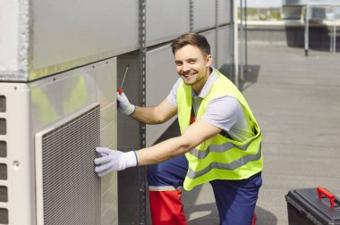 Çatıda bakım, onarım, teftiş ya da havalandırma ya da servis yapan gülümseyen bir mühendisin portresi. İşçi ekipmanların çalışmasını ve performansını güvence altına alır.