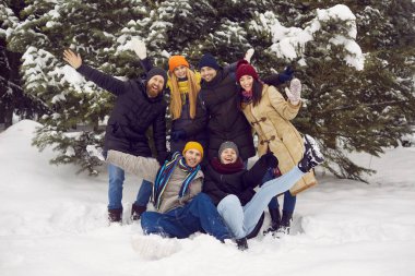 Güzel kış gününde eğlenen ve taze karın tadını çıkaran bir grup mutlu gencin portresi. Sıcak giysili gençler kameranın önünde gülüp eğleniyorlar..