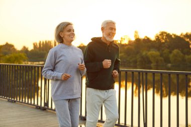 Spor kıyafetleriyle parktaki köprüde koşan ve gün batımında spor antrenmanı yapan son sınıf sporcusu bir çift. Yaşlı bir adam ve kadın dışarıda koşuyor. Emekliler konsepti için doğada yürüyüş egzersizi.