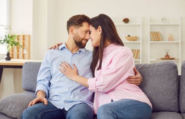 Genç mutlu çift yan yana otururken gülümsüyor, erkek kadın çift. Kanepede kucaklaşan erkek, kadın, aile tipi sağlıklı iletişim, anlayış, güçlü duygu, duygusal bağlılık.