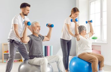 Sağlık çalışanları olgun insanların spor yapmalarına yardımcı oluyor. Spor salonundaki halterlerin üzerinde oturuyorlar. Rehabilitasyon merkezinde emekli erkek ve kadına yardım eden fizyoterapist..