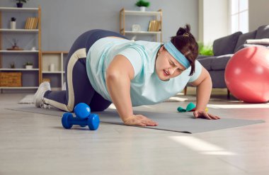 Kilolu bir kadın fitness sporlarını çok zor bulur. Yorgun, bitkin, şişman, spor giyimli genç bir kadın evdeki spor minderinde zor şınav çekmeye çalışıyor.