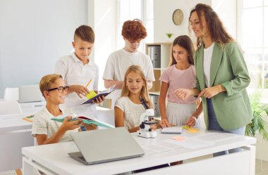Kendini adamış öğretmen, okul sınıfında öğrencilerin not defterlerini kontrol ediyor. Öğrencilerle birlikte, takım çalışmasını ve ders sırasında mükemmelliğe ortak bir bağlılığı teşvik ediyor..