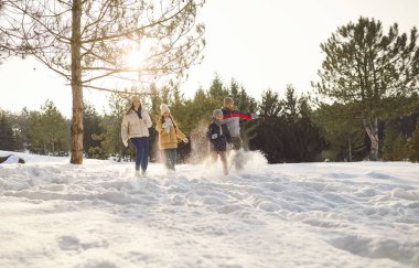 Mutlu, gülümseyen bir aile. İki çocuk ve kız kış parkında yürüyor. Güzel doğanın tadını çıkarıyorlar. Anne, baba ve çocukları ormanda birlikte zaman geçiriyorlar.