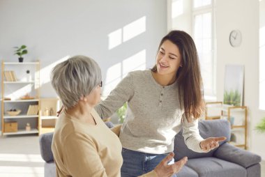 Mutlu gülümseyen yetişkin kızı, oturma odasında bir arada duran yaşlı gri saçlı annesine sarılıyor. Bir kadın, eski ailesini evinde ziyaret ediyor. Aşk, aile eğlencesi ve anneler günü konsepti..
