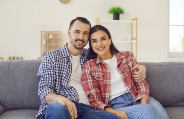 Evdeki kanepede mutlu bir ailenin portresi. Karı ve kocayı seven, ekose gömlekli, kanepede oturan, kameraya bakan ve gülümseyen.