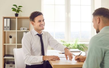 Dost canlısı gülümseyen adam iş danışmanı, emlakçı, borsacı, girişimci, yönetici müşterisiyle ya da meslektaşıyla görüşür, bir anlaşma yapar ve sözleşme imzalarlar.