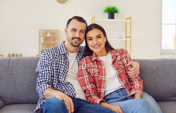 Портрет счастливой семейной пары на диване дома. Любимые муж и жена в повседневной клетчатой и клетчатой рубашки, сидя вместе на диване, глядя в камеру и улыбаясь