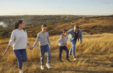 Mutlu aile gün batımında sarı tarlada teselli ve neşe bulur. Işıldayan ebeveynler, keyifli çocuklarını izliyor. Doğadaki aile, doğa oyununun basit zevkleri. Doğadaki aile.