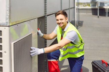 Çatıda bakım, onarım, teftiş ya da havalandırma ya da servis yapan gülümseyen bir mühendisin portresi. İşçi ekipmanların çalışmasını ve performansını güvence altına alır.