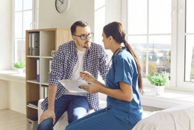 Tıp doktorluğundaki genç bir hastanın portresi klinikteki muayene sırasında elinde randevu ve danışmanlık ile rapor tutan dost canlısı bir kadın hemşireyi dinliyor..