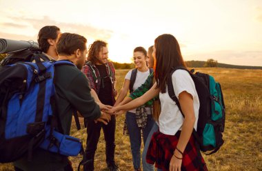 Mutlu turistler el ele tutuşuyor. Sırt çantalı, güz tarlasında el ele tutuşup el ele tutuşan bir grup neşeli erkek ve kadın arkadaş. Turizm, yürüyüş, eğlence, takım çalışması konsepti