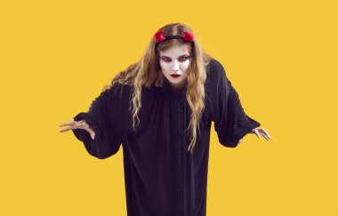 Sarı arka planda şeytani kılık değiştirmiş genç bir kız. Cadılar Bayramı kostümü giymiş bir kadın saldırmaya hazırlanıyor ve ciddi bir hipnotize edici yüz ifadesiyle kameraya bakıyor.