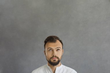 Ciddi bir gencin portresi. Metin için fotokopi odasına bakıyor. Yakışıklı sakallı adam tercihleri düşünüyor ya da gri bir arka planda bir şeyler hayal ediyor.