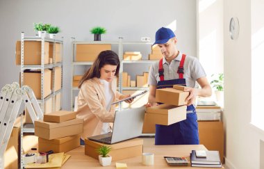 Depoda lojistik ya da dağıtım merkezindeki kadın küçük işletme sahibiyle çalışan teslimat işçisi bir müşterinin siparişini hazırlıyor. Stok envanteri.