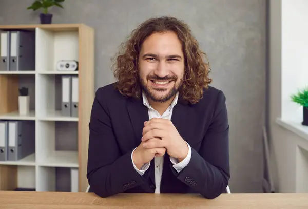 stock image Portrait of businessman attending work meeting via video call. Webcam view head shot portrait of happy young long haired business man in suit sitting at office desk, looking at camera and smiling