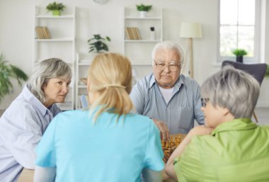 Genç kadın hemşire ya da bakıcıyla satranç oynayan bir grup yaşlı erkek ve kadın huzurevinde oturmuş masada eğleniyorlar. Huzurevi konseptinde boş zaman.