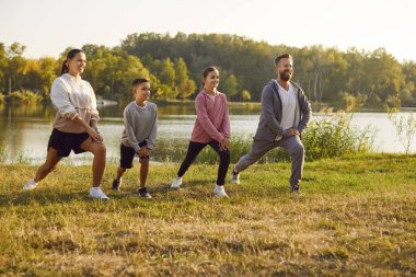 İki çocuklu, sportif ve mutlu bir aile, doğada spor egzersizleri yapıyor. Spor giyim kuşamında gülümseyen aile parkta antrenman yapıyor. Açık hava eğitimi ve spor konsepti.