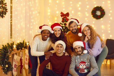 Noel Baba şapkalı gülümseyen çoklu etnik arkadaşların grup portresi yeni yıl filmi için birlikte poz veriyor. Çeşitli uluslar arası gençler Noel 'i süslü evlerinde kutluyor. Kış tatili.