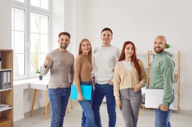 Bir grup genç kadın ve erkek kameraya bakıyor ve ofiste gülümsüyor. Çalışanların takımı, şirket çalışanları ya da bir grup öğrencinin güvenli ve neşeli bir şekilde sıraya girmesi..