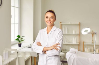 Gülümseyen genç bir kadın kozmetik uzmanı ya da güzellik salonu ofisinde kameraya neşeli bir şekilde bakan güzellik uzmanı portresi. Kozmetoloji ve cilt bakımı.