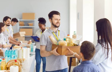 Mutlu erkek gönüllü bir mülteci ailesine, anne ve oğluna sosyal yardım merkezinde bir yiyecek kutusu vererek yardım ediyor. Sadaka, kamu hizmeti ve ihtiyacı olanlara yardım etme azmi..