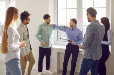 Bir grup mutlu, gülümseyen, etnik çeşitlilikte iş adamı toplantıdan sonra sohbet ediyor. İş arkadaşları ya da şirket çalışanları resmi olmayan bir ortamda ofiste çember oluşturup konuşuyorlar. Takım çalışması konsepti.