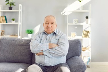 Oturma odasındaki koltukta oturan, kollarını kavuşturup kameraya bakan kendinden emin yaşlı bir adamın portresi. Kır saçlı, gömlek giyen, koltukta oturan son sınıf öğrencisi..