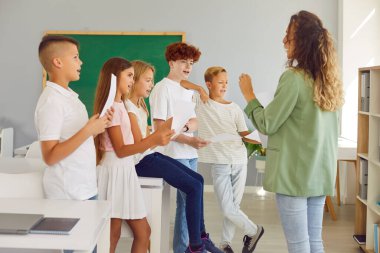 Çeşitli öğrencilerden oluşan bir grup ile birlikte bir okul sınıfında müzik dersi sırasında şarkı söyleyen bayan öğretmen. İlgi çekici sınıf, müzik ve işbirlikçi öğrenmeyi teşvik eder..