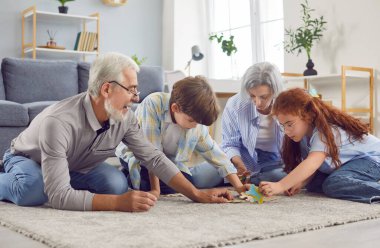 Büyükanne, büyükbaba ve torunların aileleri evdeki oturma odasında bir yapbozun içinde yerde oynuyorlar. Gülen yaşlı çift çocuklarla yapboz topluyor. Aile eğlencesi ve insan konsepti.
