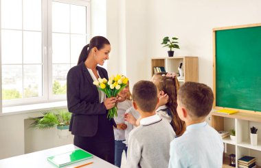 Küçük sevimli okul çocukları sevgili bayan öğretmenlerini tebrik ediyor ve tatil için sınıfa gitmeden önce çiçeklere sarı lale buketi veriyorlar. Çocuklar okula geri dönsün