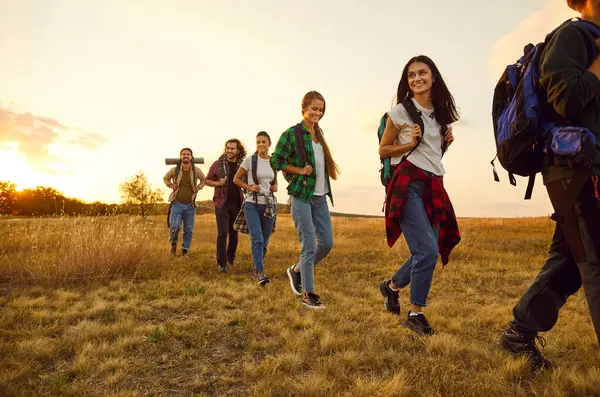 Genç mutlu turistler, büyük sırt çantalarıyla doğada yürüyüş yapıyorlar ve sahada birlikte yürüyorlar. Güler yüzlü arkadaşlar dışarıda yürüyüş yapıyorlar. Macera, seyahat ve turizm konsepti.