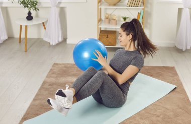 Egzersiz yapan güzel bir genç kız evde spor topuyla yoga minderinde yatıyor. Sportif Kafkasyalı kız fitball oynayarak Rusça kıvırıyor. Sağlıklı bir yaşam tarzı sürdürme kavramı.