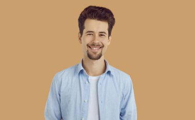 Mavi tişörtlü, bej arka planda kameraya bakan mutlu, sakallı esmer adamın portresi. Reklam ve pazarlama afişi. Samimi duygular konsepti. Genç yakışıklı adamın stüdyo fotoğrafı..