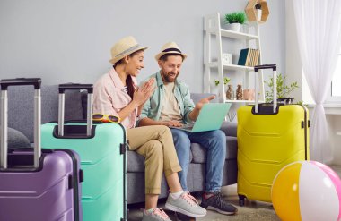 Mutlu gülümseyen çift koltukta bavullarıyla oturuyor ve dizüstü bilgisayarla bilet ayırtıyorlar. Plaj şapkası takan genç bir adam ve kadın tatil gezisine hazırlanıyor. Tatil kavramı.